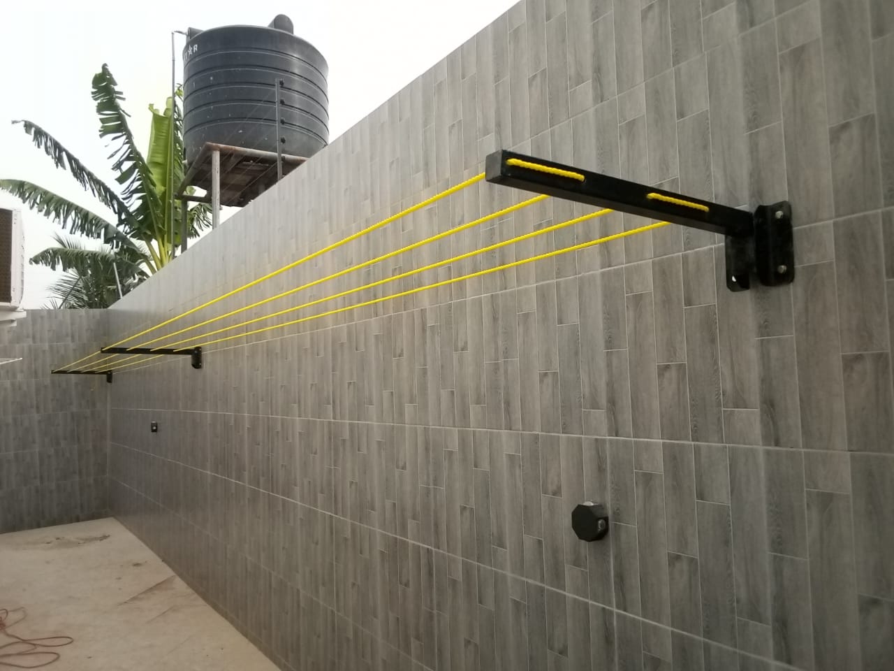 Foldable drying line open along a tiled compound wall beneath a raised polytank