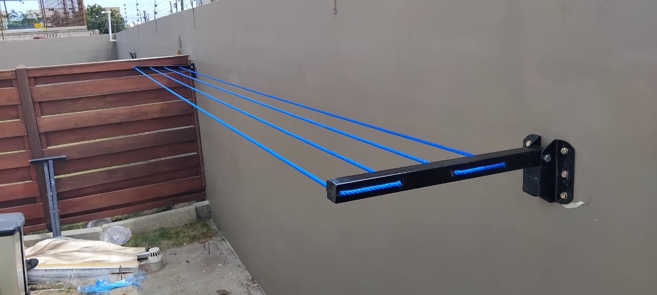 Foldable drying line installed on a compound wall next to a slatted timber fence