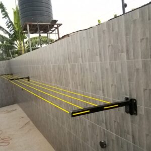 Wall-mounted foldable drying line open across a tiled compound wall in Accra, amber lines strung between the arms