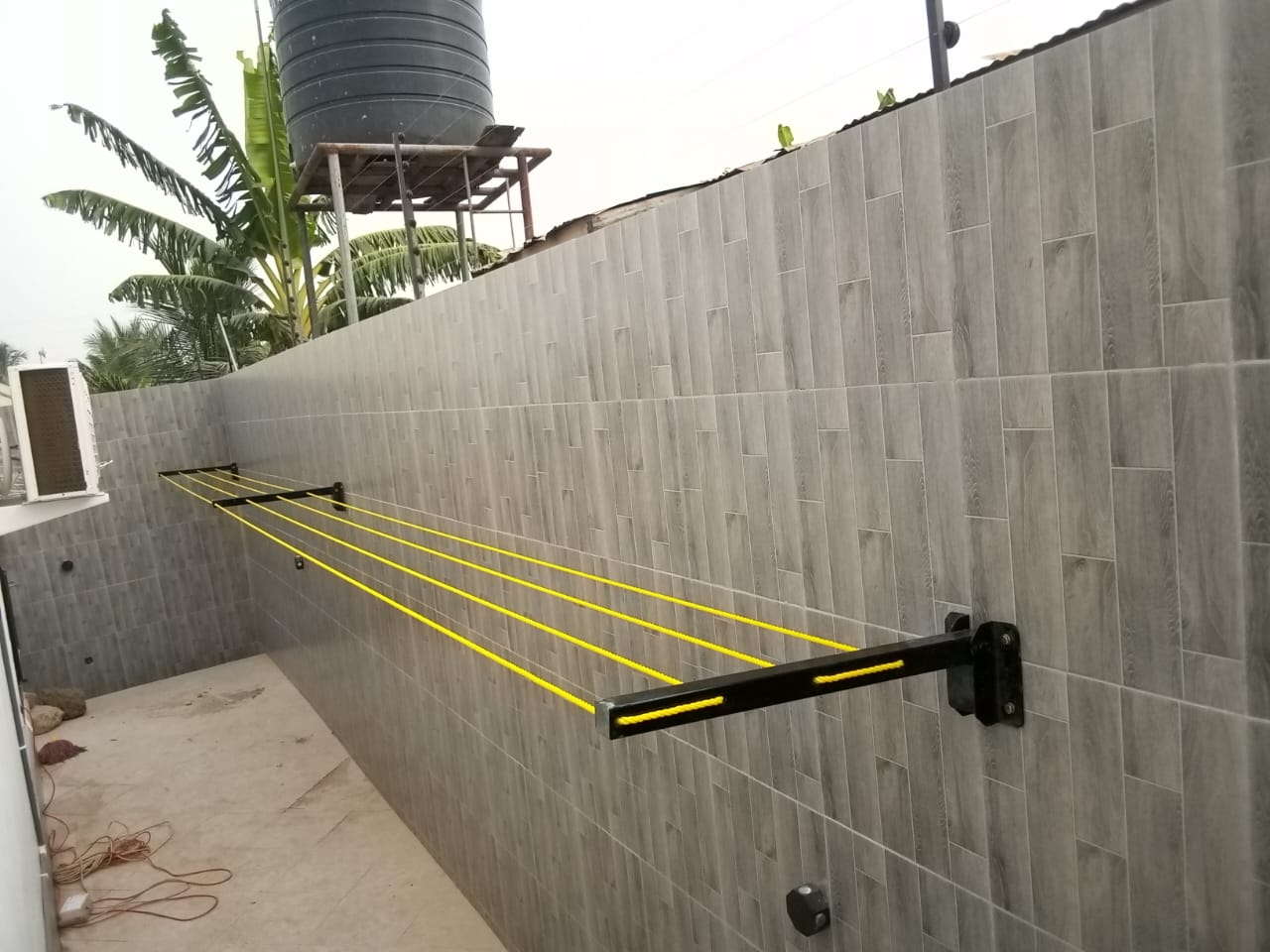 Wall-mounted foldable drying line open across a tiled compound wall in Accra, amber lines strung between the arms