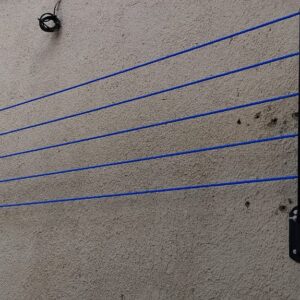 Six blue drying lines strung across a plastered wall from a black wall-mounted foldable arm